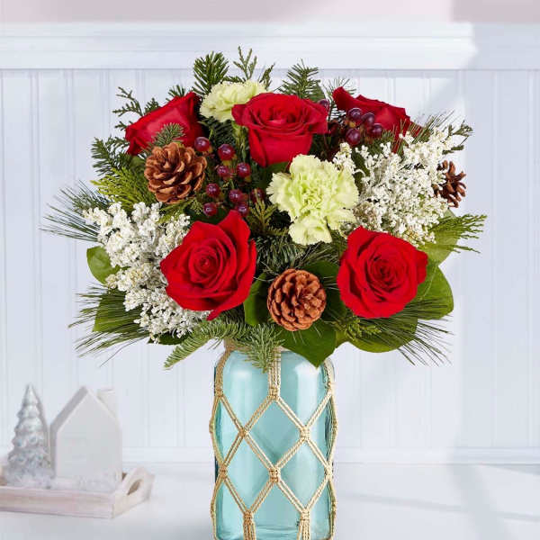 Red roses and white carnations in a blue glass vase with pinecones