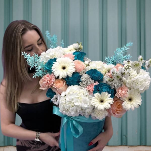 Woman holding a large bouquet in a blue box with white, peach, and teal flowers