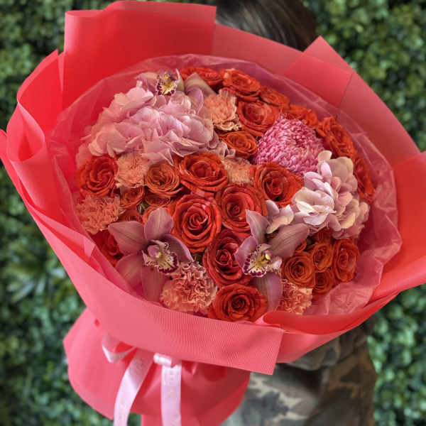 Large bouquet of red and pink roses with orchids wrapped in bright pink paper