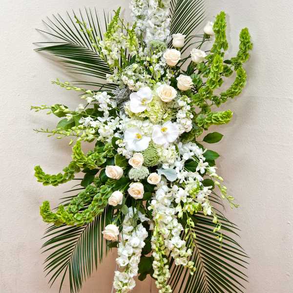 Tall white floral arrangement with roses, orchids, and palm fronds