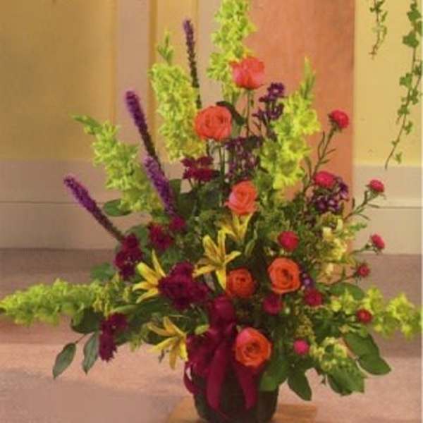 Tall mixed flower arrangement with orange roses and purple spikes in a vase