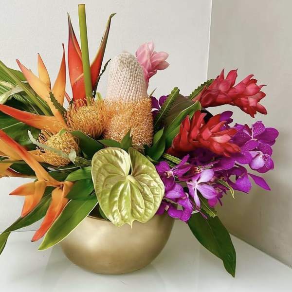 Tropical flower arrangement in a gold bowl with orange, red, pink, and purple blooms