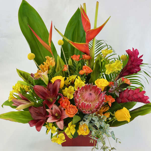 Tall tropical arrangement with red lilies, protea, roses, and yellow blooms in a red container