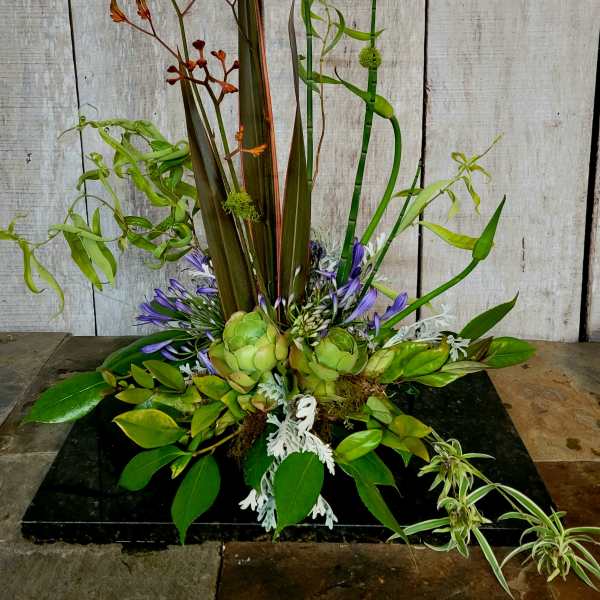 Tall tropical arrangement with green succulents and purple flowers on a black base