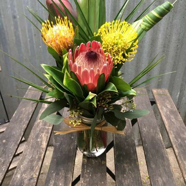 Tropical-style bouquet with pink and yellow protea in a clear glass jar vase