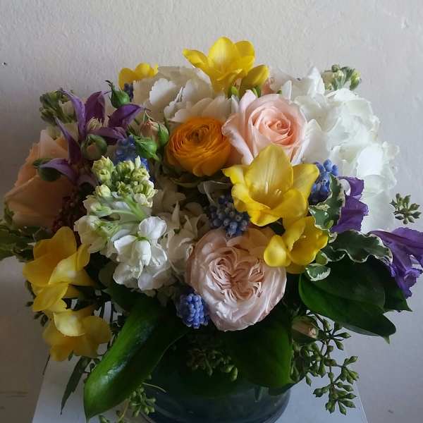 Mixed bouquet of yellow, white, pink, and purple flowers in a dark vase
