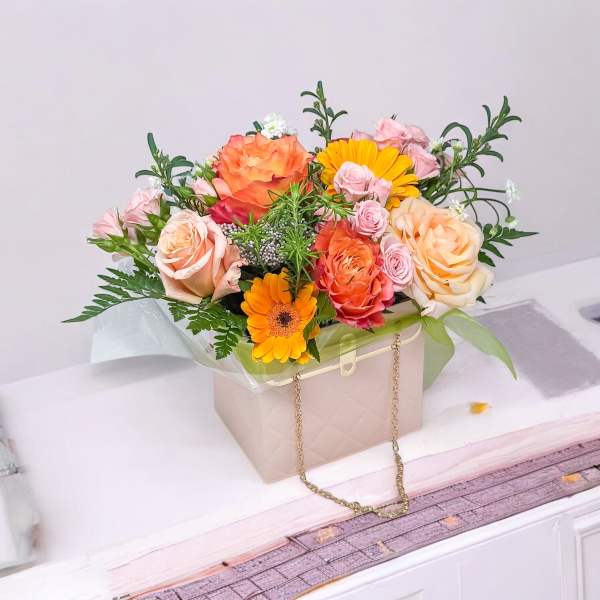 Mixed bouquet of peach, pink, and orange flowers in a beige gift box