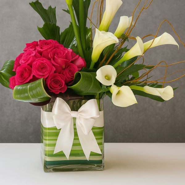 Pink roses and white calla lilies in a glass vase with a white bow