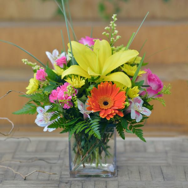 Mixed bouquet with yellow lilies, orange gerbera daisy, and pink flowers in a glass vase