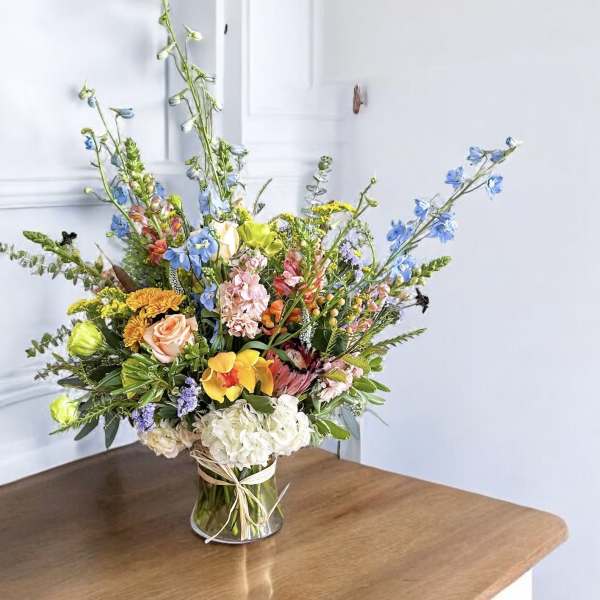 Tall mixed bouquet in a clear glass vase with blue and peach flowers