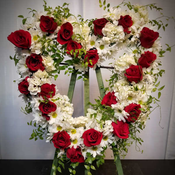 Heart-shaped floral wreath with red roses and white daisies on a stand