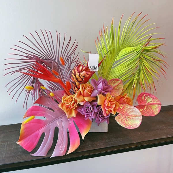 Tropical floral arrangement with orange and purple roses and colorful palm leaves