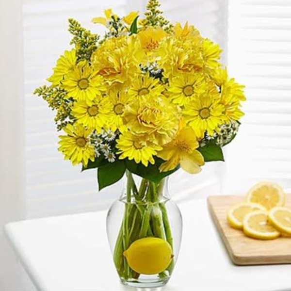 Yellow flower bouquet in a clear glass vase with a lemon inside