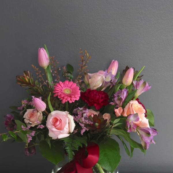 Pink roses and mixed blooms arranged in a glass vase with a red ribbon
