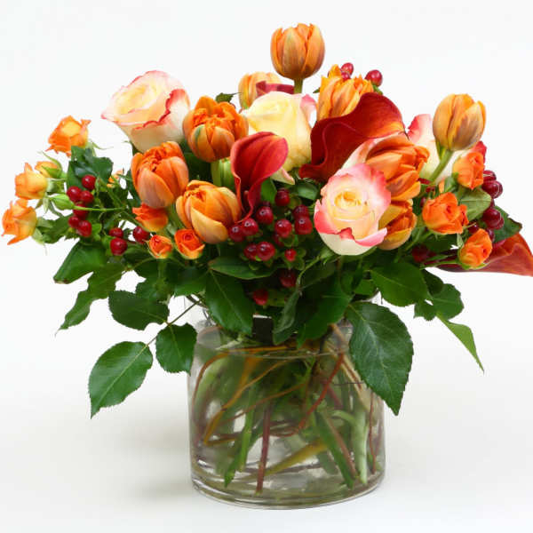 Orange and cream tulips with red berries in a glass vase