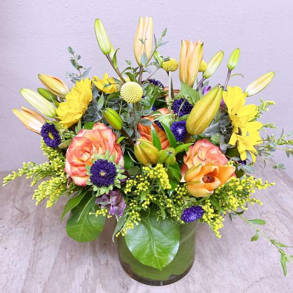 Mixed bouquet of lilies, roses, and yellow daisies in a glass vase