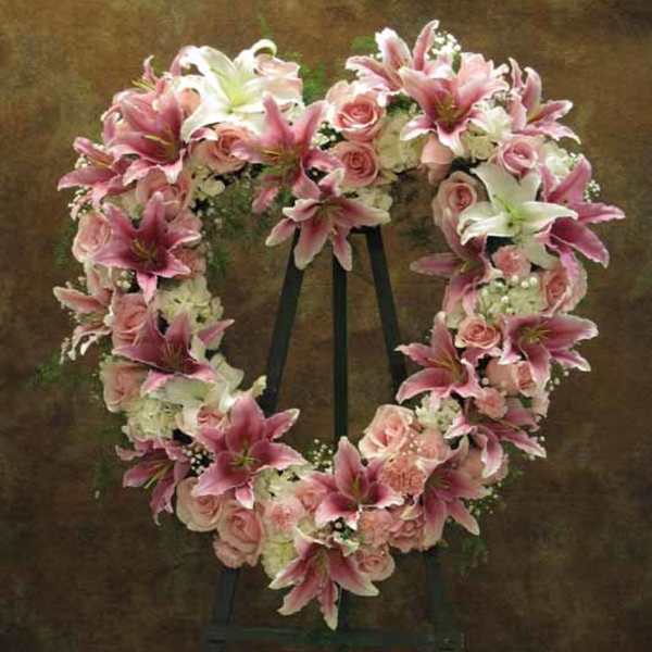 Heart-shaped floral wreath with pink lilies and roses on an easel