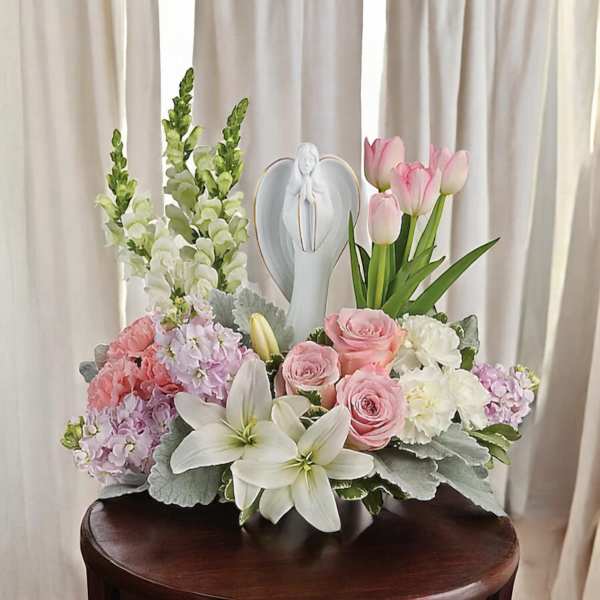 Pink tulips and roses arranged with white lilies and a figurine centerpiece