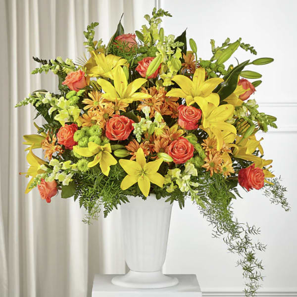 Bright mixed bouquet in a white pedestal vase with yellow lilies and orange roses
