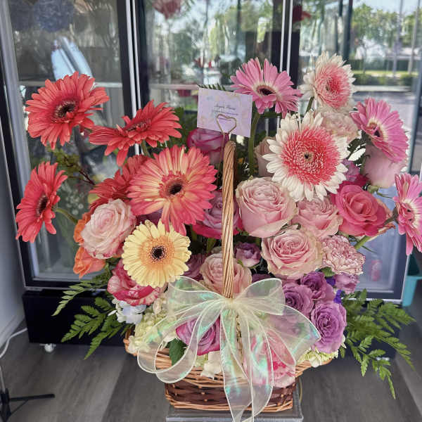 Basket arrangement of pink gerberas and roses with a sheer bow
