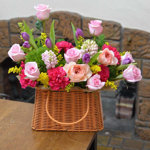 Basket arrangement of pink and peach roses with purple tulips and carnations