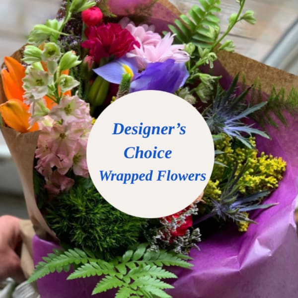 Wrapped bouquet of mixed colorful flowers with a designer's choice label