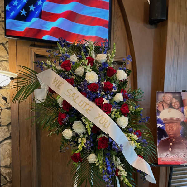 Standing floral tribute with red and white roses and a white ribbon reading "We salute you"