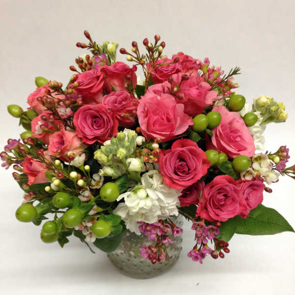 Pink rose bouquet in a textured glass vase with white blooms and green berries