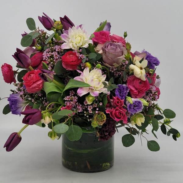 Lush arrangement of pink, purple and white mixed flowers in a clear glass vase