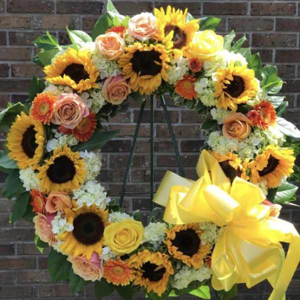 Standing wreath of sunflowers, roses, and other bright blooms with a large yellow bow on an easel