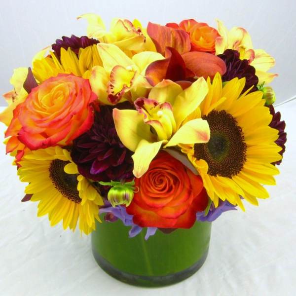 Bright bouquet of sunflowers, roses, and orchids in a green vase