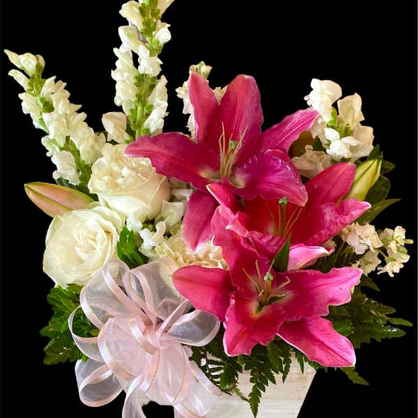 Pink lilies and white roses in a white container with a ribbon bow