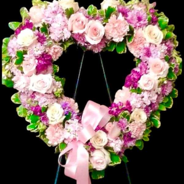 Heart-shaped floral wreath with pink roses and a pink ribbon on a stand