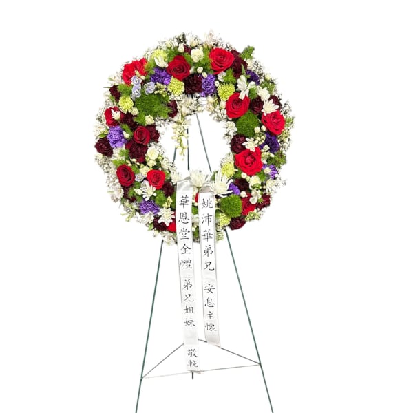 Circular funeral wreath of red, white, purple, and green flowers on a stand