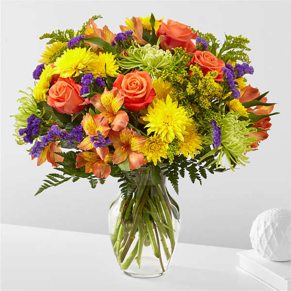 Bright mixed bouquet of roses, daisies, and purple accents in a glass vase