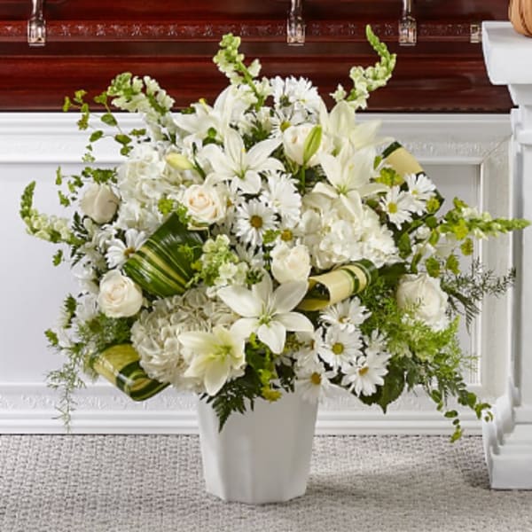 White floral arrangement in a white vase with lilies, roses, and daisies