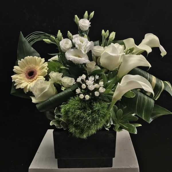 White floral arrangement with calla lilies, roses, and a gerbera daisy in a black vase