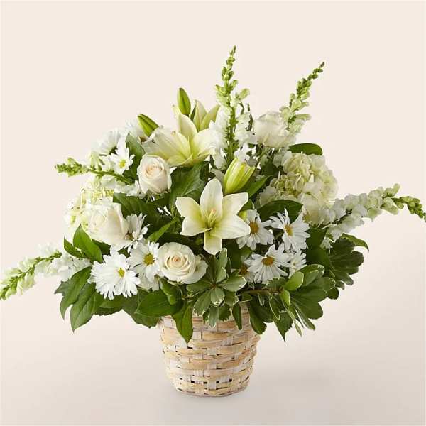 White lilies, roses, and daisies arranged in a woven basket with lush foliage