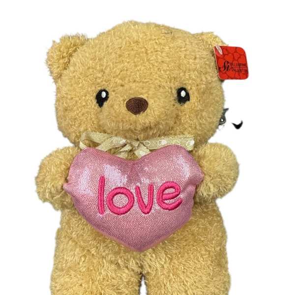 Plush teddy bear holding a pink heart with the word love