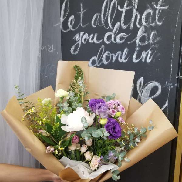 Hand-tied bouquet of purple, white, and pink flowers in brown paper