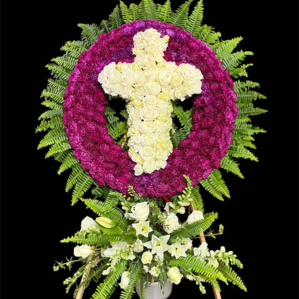 Floral standing tribute with a white cross in a magenta wreath