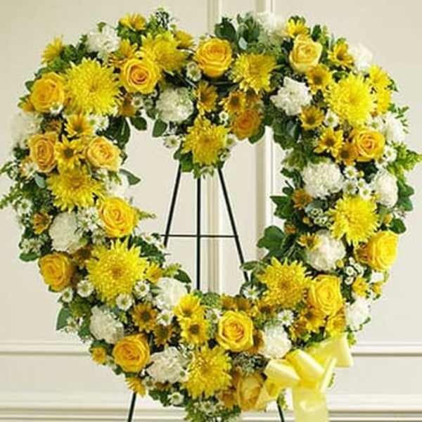 Heart-shaped standing wreath of yellow roses and white flowers with yellow bow on an easel