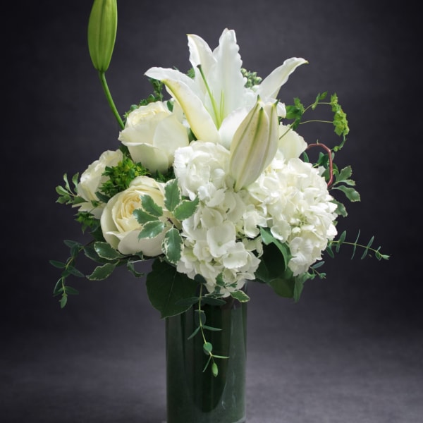 White lilies and roses arranged in a tall glass vase