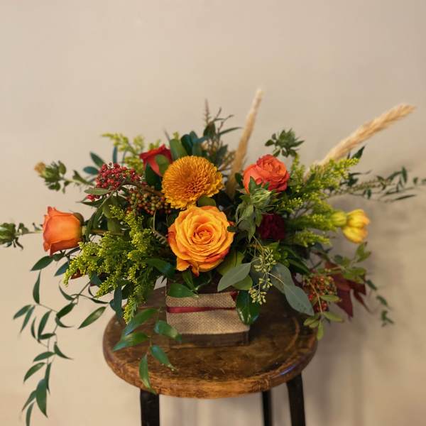 Orange and red roses in a square container with greenery