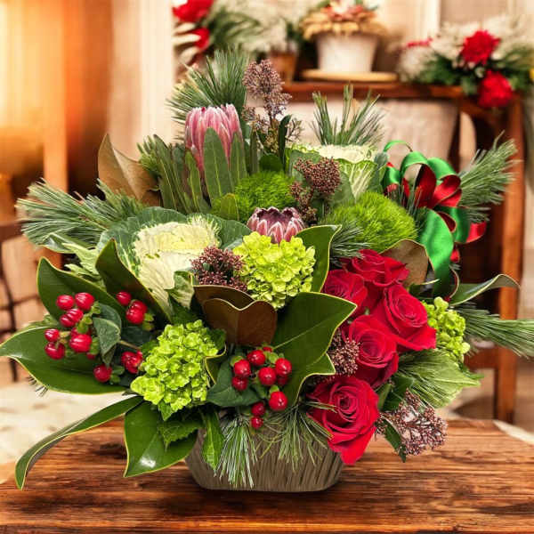 Mixed floral arrangement with red roses and green blooms in a low container