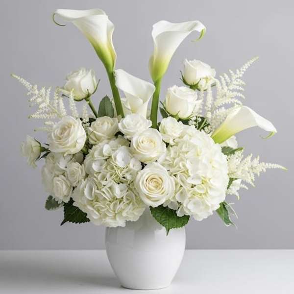 White calla lilies and roses arranged in a white vase
