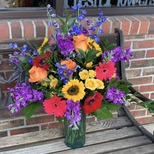 Colorful mixed bouquet in a glass vase with roses, gerbera daisies, and poppies