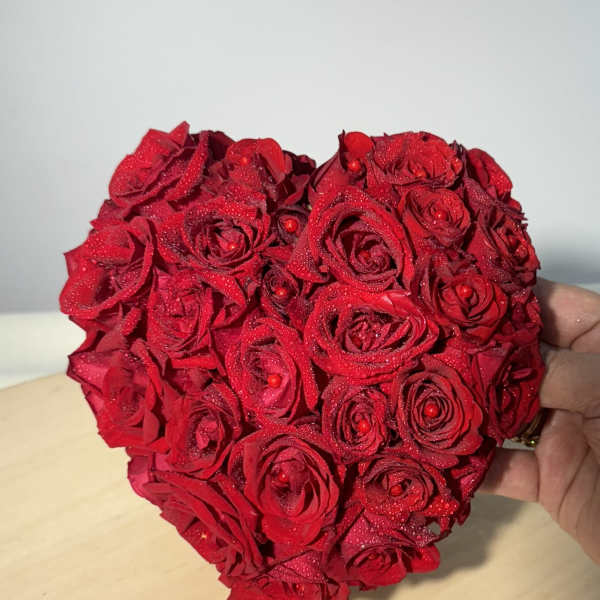 Heart-shaped arrangement of red roses held in a hand