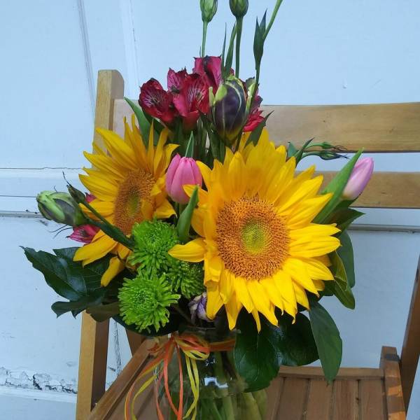 Bouquet of sunflowers, pink tulips, and red alstroemeria in a glass vase