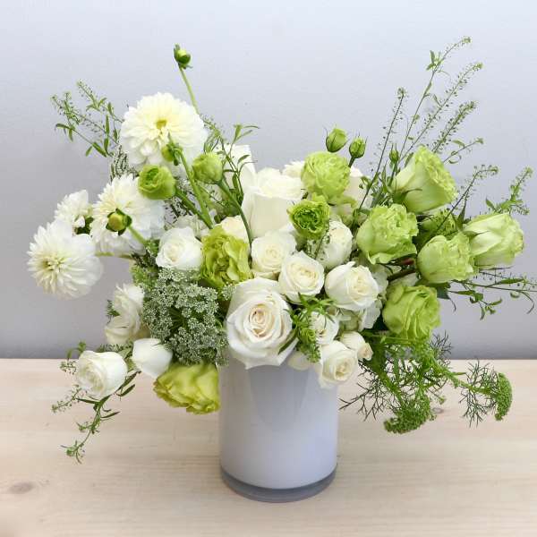 Asymmetrical white and green flower arrangement in a white cylinder vase